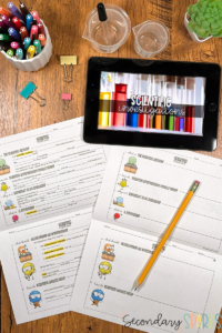 iPad on a table featuring Scientific Investigations Powerpoint lesson. Two pages of guided notes withcolorful characters. Plant, paper clips and a pencil.